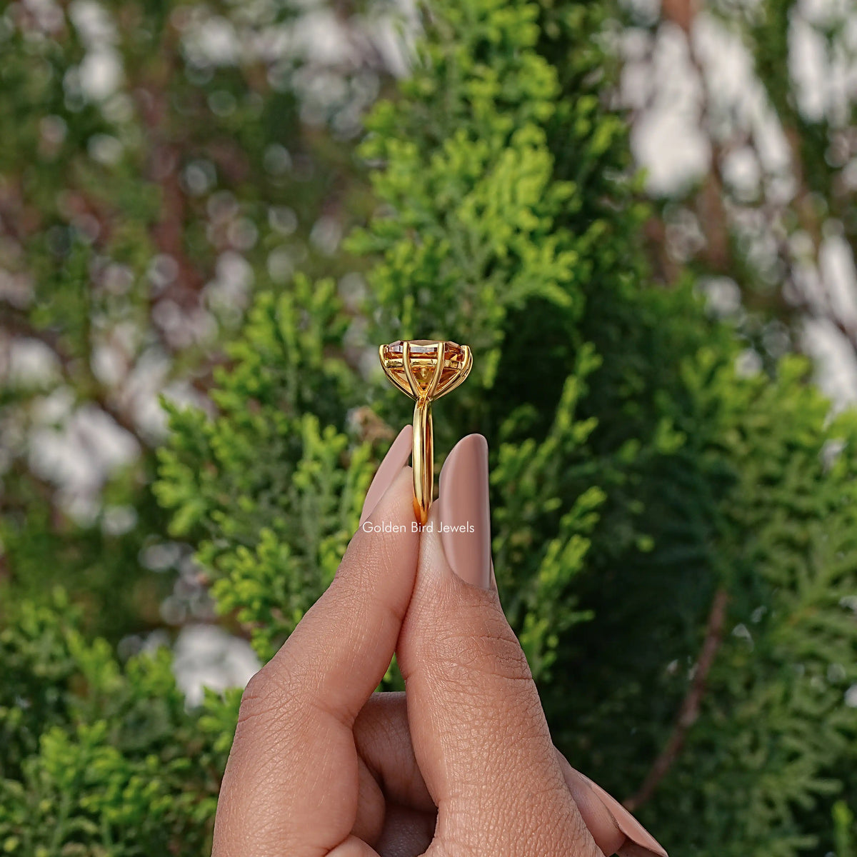 Gold-toned cushion-cut moissanite engagement ring held between fingers