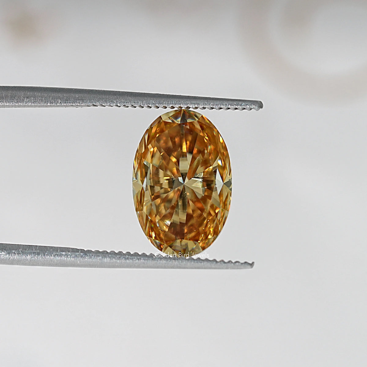 Oval champagne moissanite loose stone held in tweezers, bright golden center