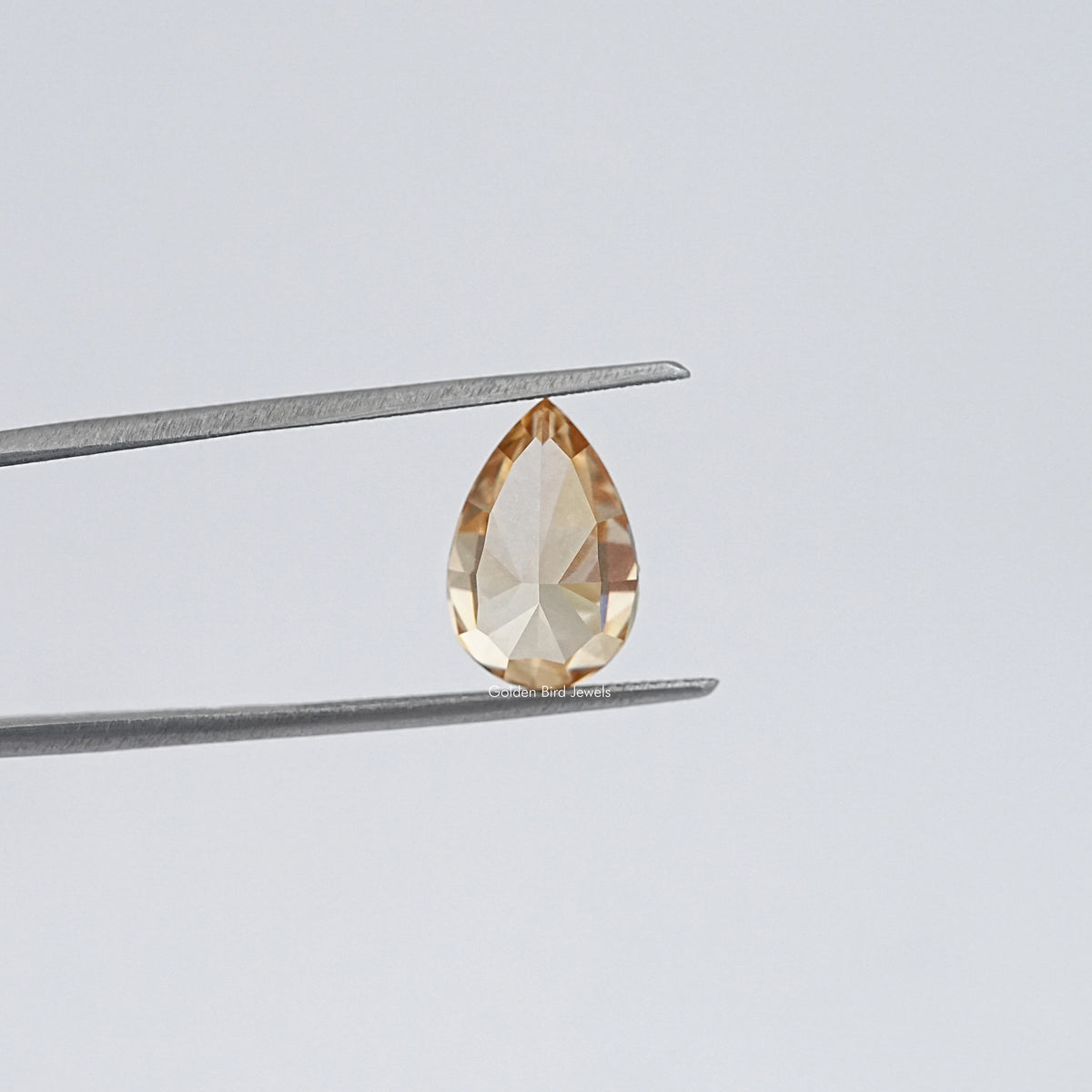 Pear-cut moissanite loose stone held by tweezers, golden champagne, close-up