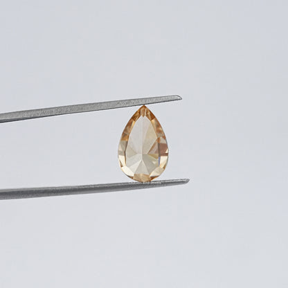 Pear-cut moissanite loose stone held by tweezers, golden champagne, close-up