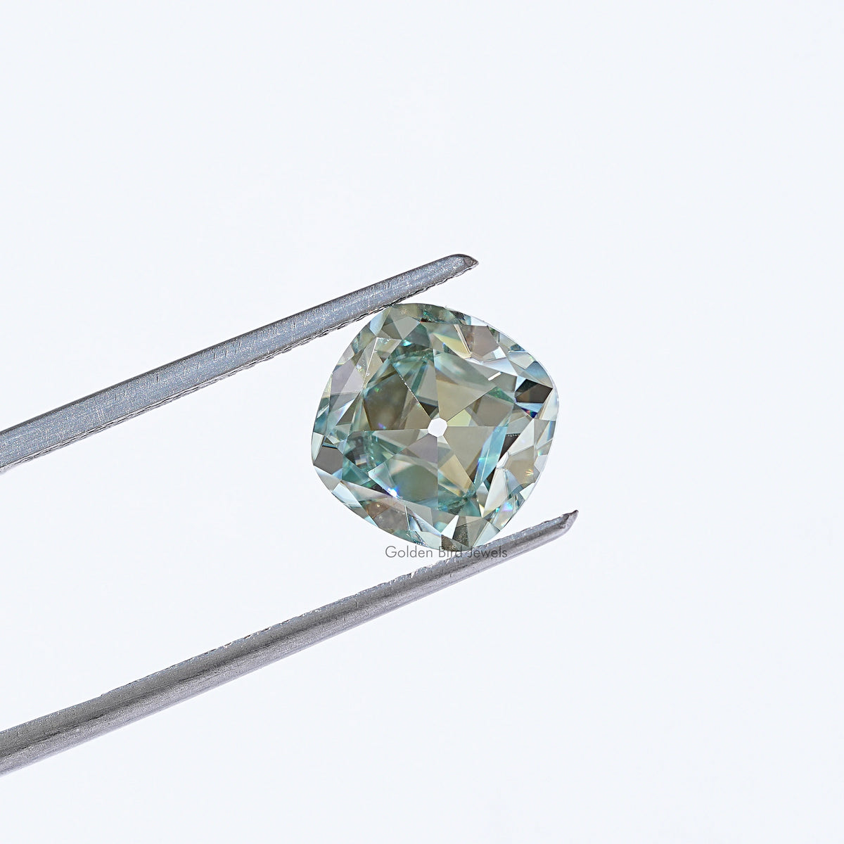 Light blue moissanite gemstone in silver tweezers, cushion old mine cut