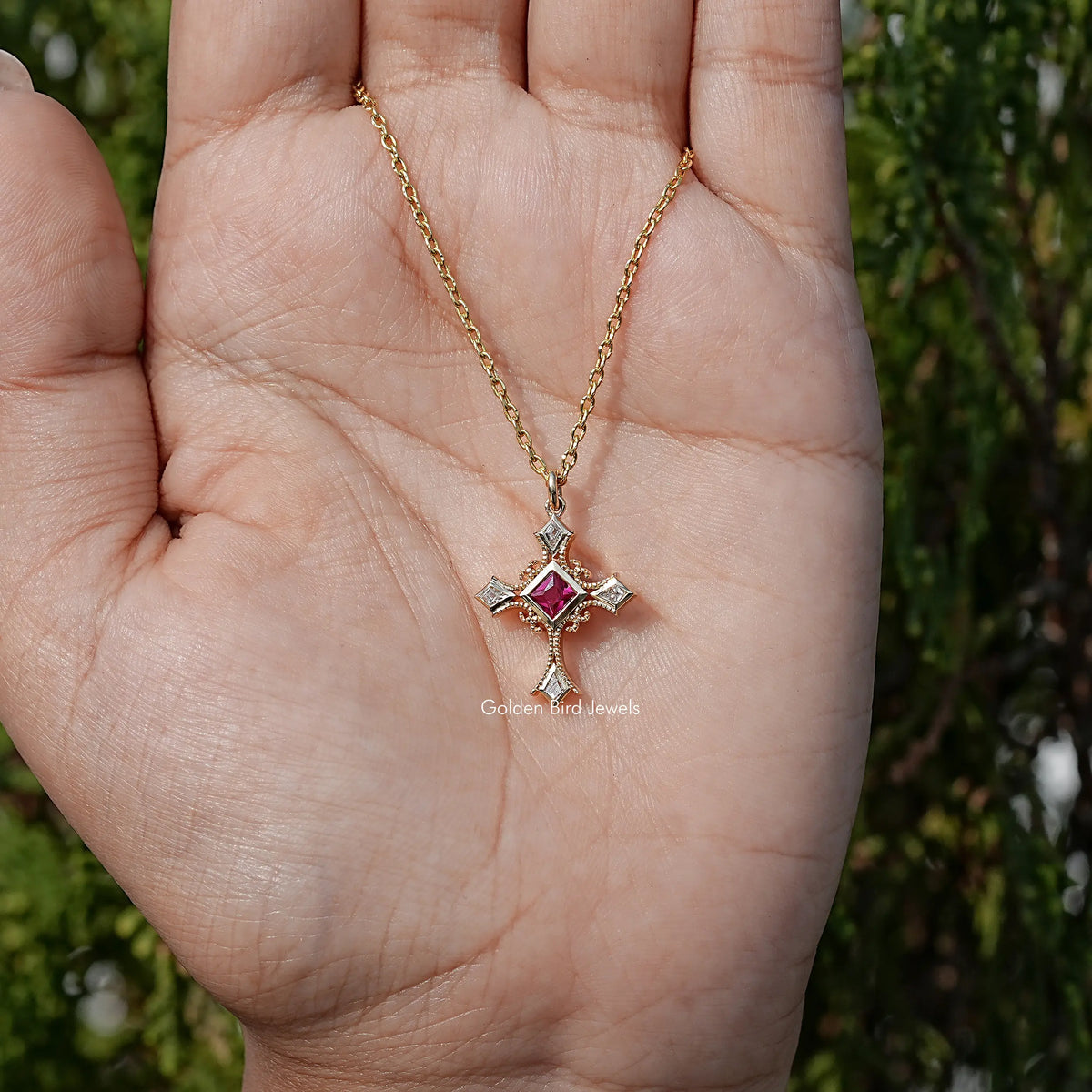 Gemstone cross pendant necklace on open palm; square red center with silver prongs