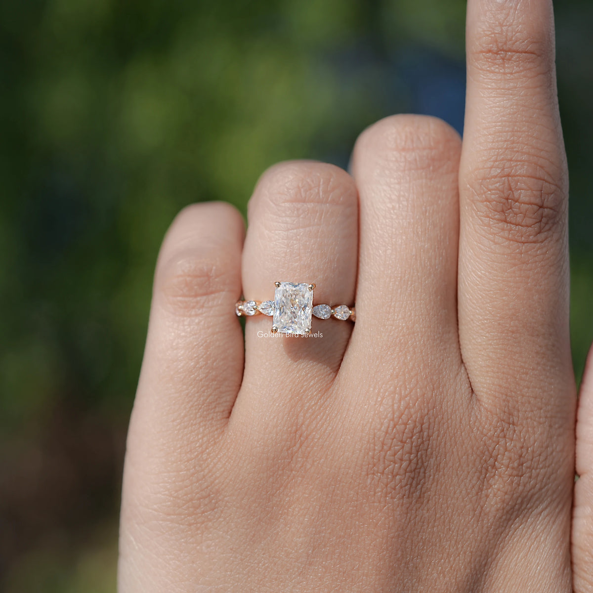 Silver-tone three-stone style radiant-cut halo ring with round accent stones.