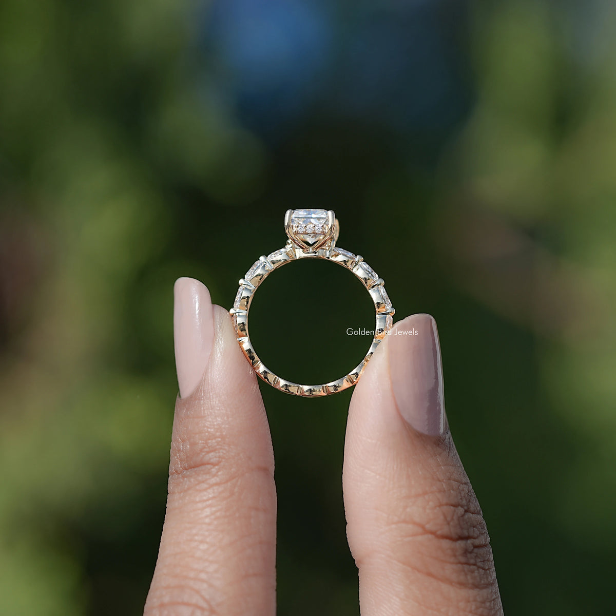Silver-tone radiant-cut halo moissanite ring with side stones, held in hands.