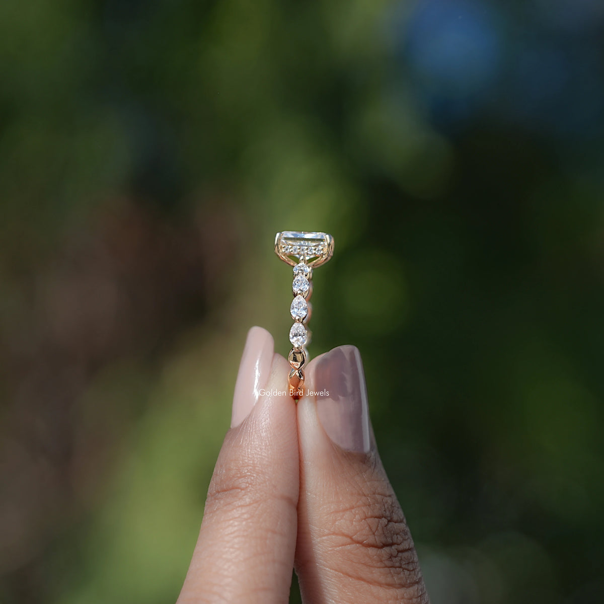 Radiant-cut halo moissanite ring with prong-set center and dangling sparkle stones.