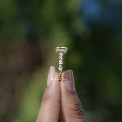 Radiant-cut halo moissanite ring with prong-set center and dangling sparkle stones.