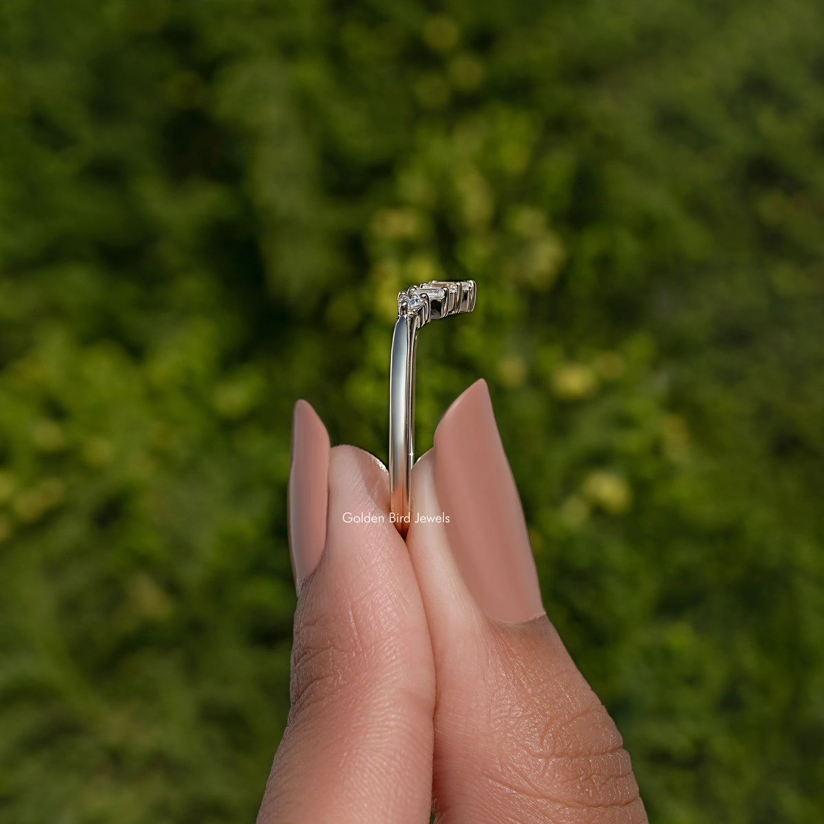 Curved wedding band ring side view with baguette-cut stones, held by fingertips
