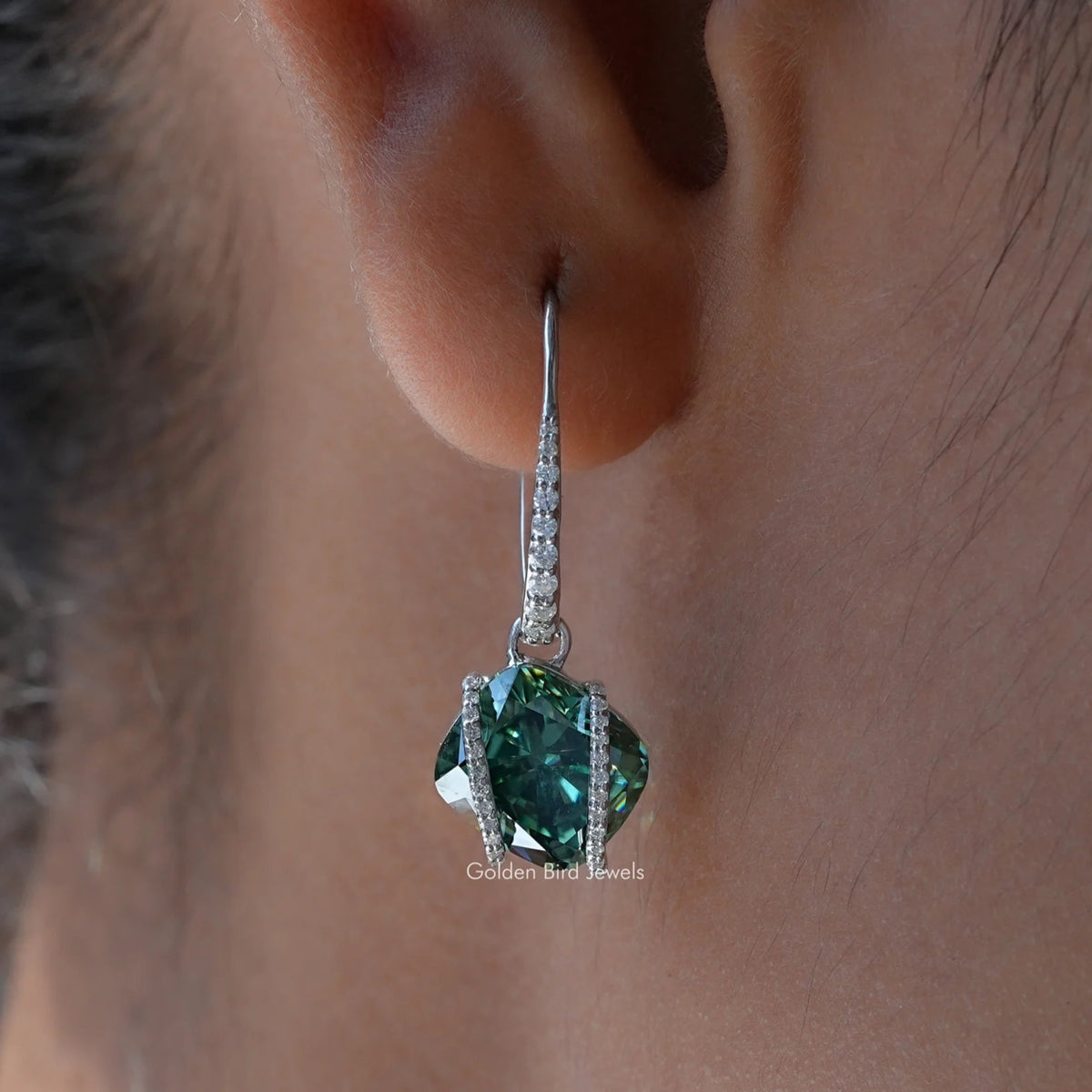 Close-up of sterling silver dangle earring with emerald-green cushion-cut moissanite