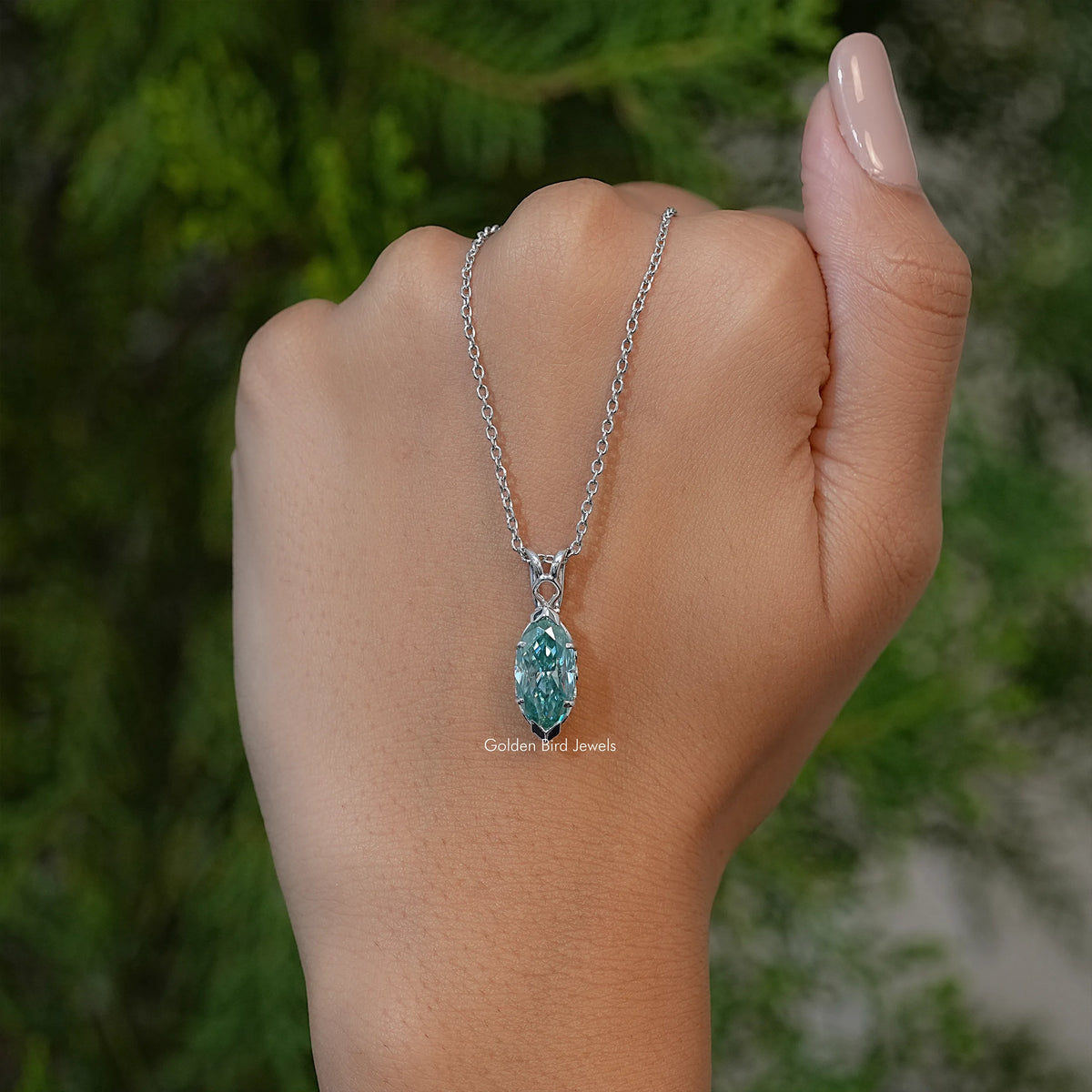 Marquise-cut green solitaire pendant necklace on silver chain, shown on upturned wrist