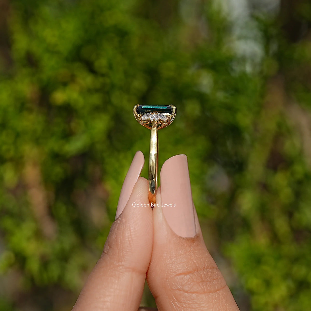 Gold engagement ring side view with dark green emerald-cut gemstone and prongs