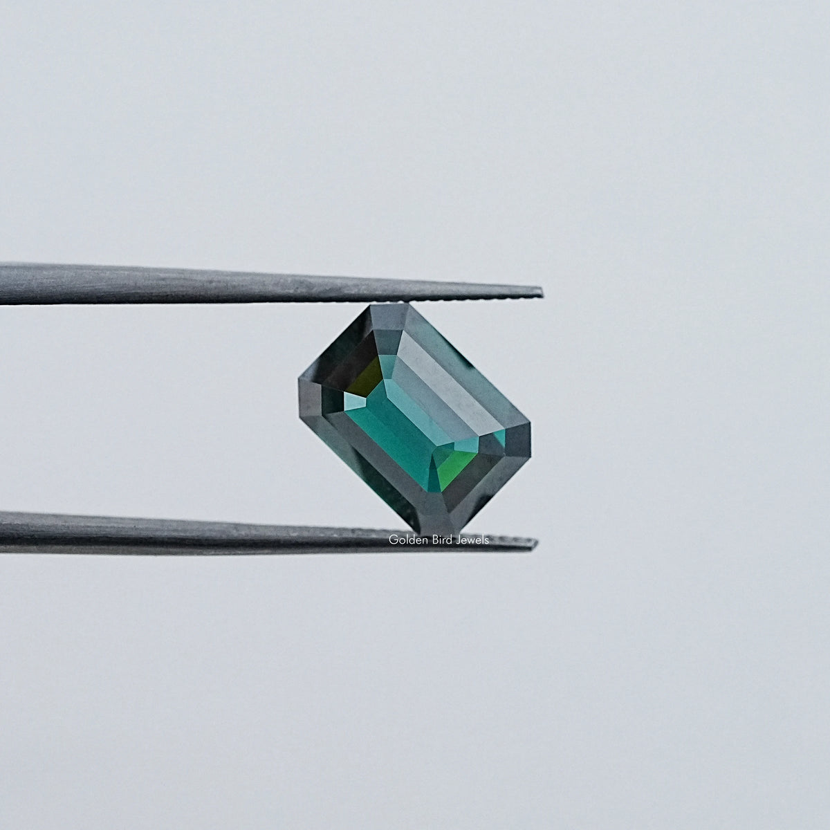 Loose emerald-cut dark green moissanite gemstone, angled view with crisp facets