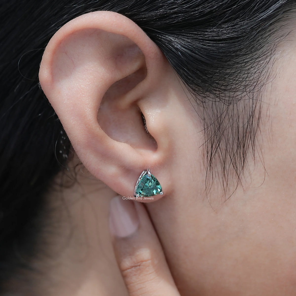 Trillion-cut dark green moissanite stud earrings on the ear, side profile