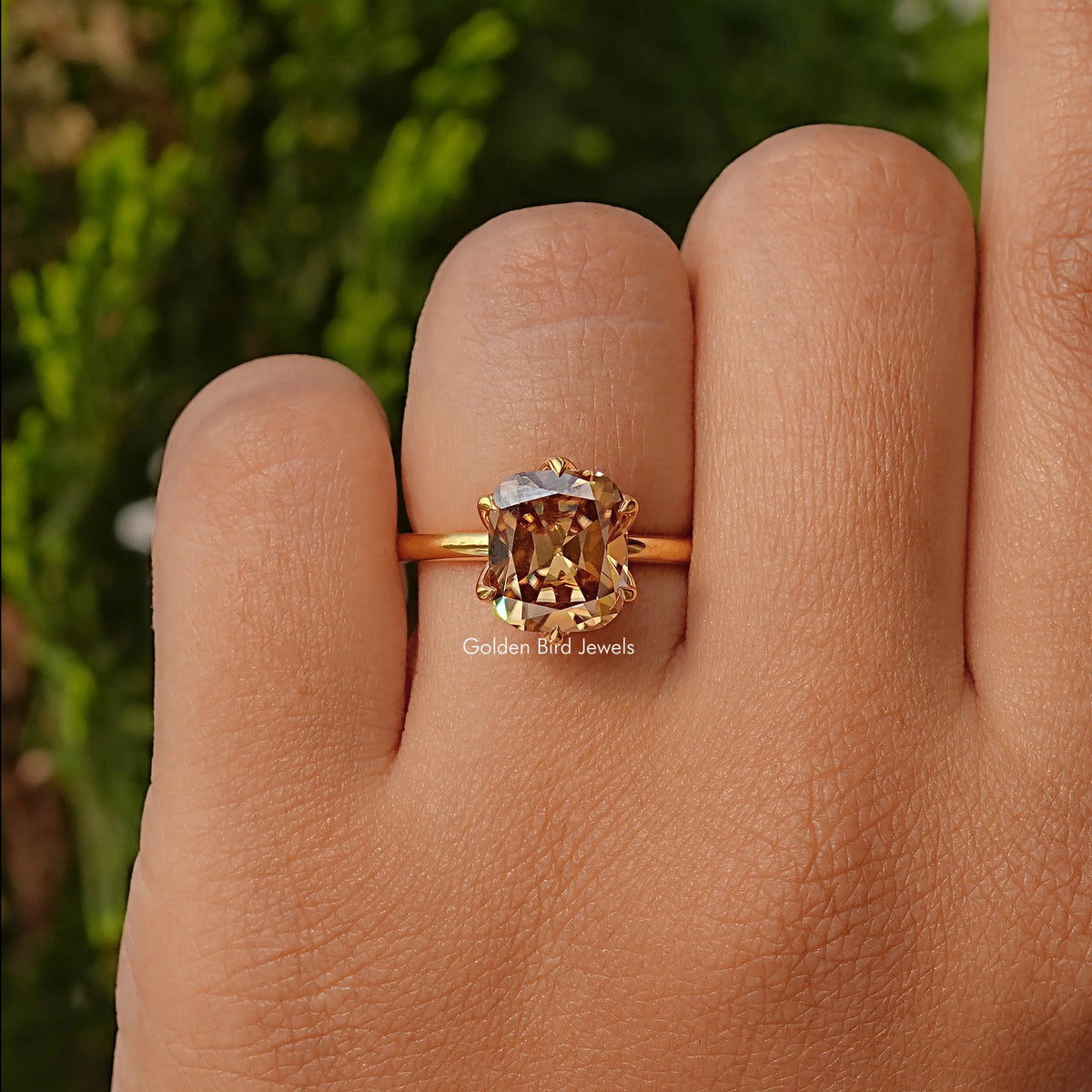 Gold band cushion-cut solitaire ring with pronged gemstone, close-up on hand