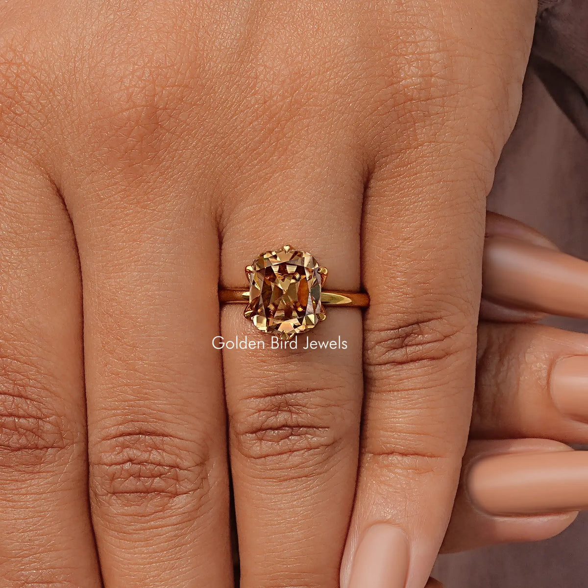 Gold tone cushion-cut solitaire ring with prong-set center stone on finger