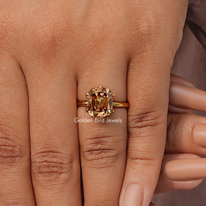 Gold tone cushion-cut solitaire ring with prong-set center stone on finger