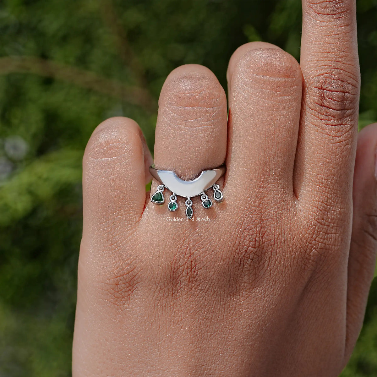 Curved bezel-set engagement ring with small green bezel-set stones, silver band