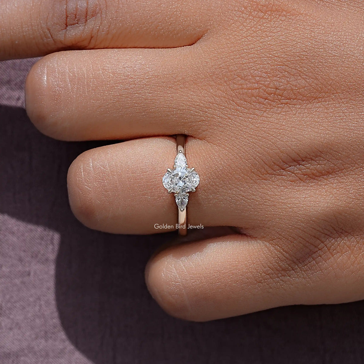 Three-stone lab-grown diamond ring on finger, round center stone with two side stones