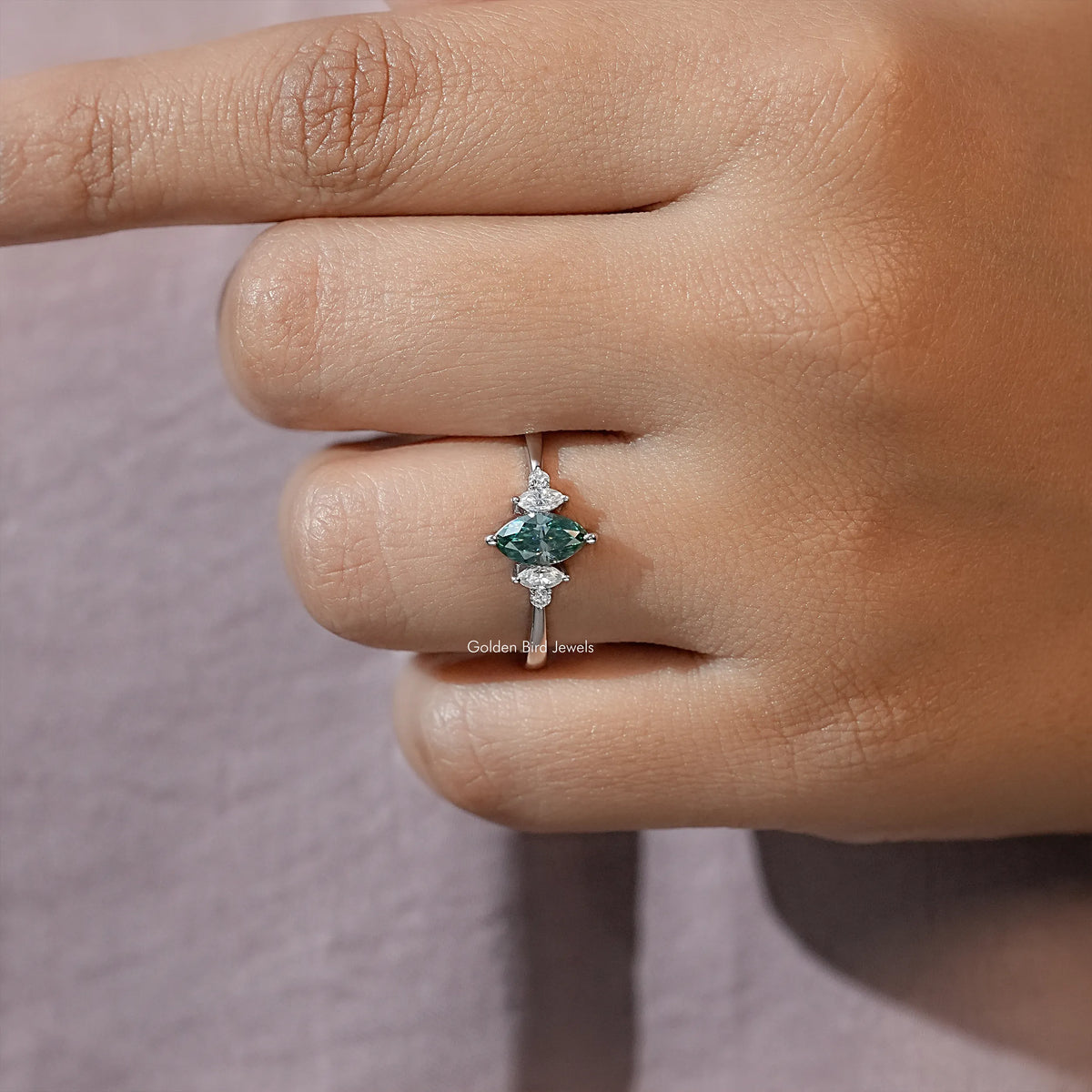 Three-stone engagement ring close-up, green marquise center with two smaller side stones