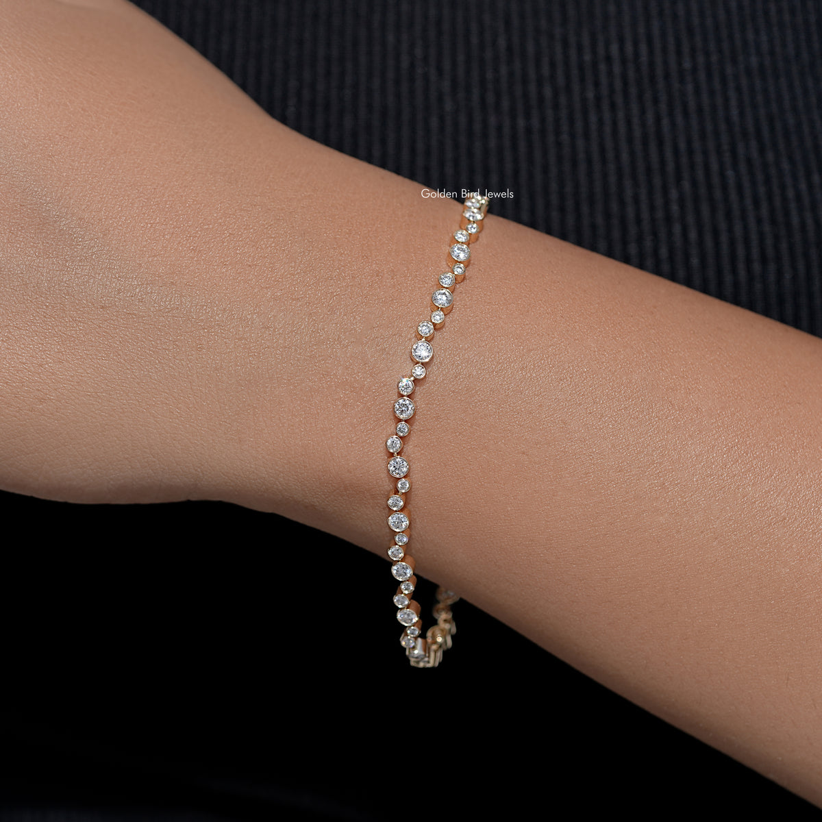 Gold-tone tennis bracelet with round bezel-set lab diamonds, wrist close-up