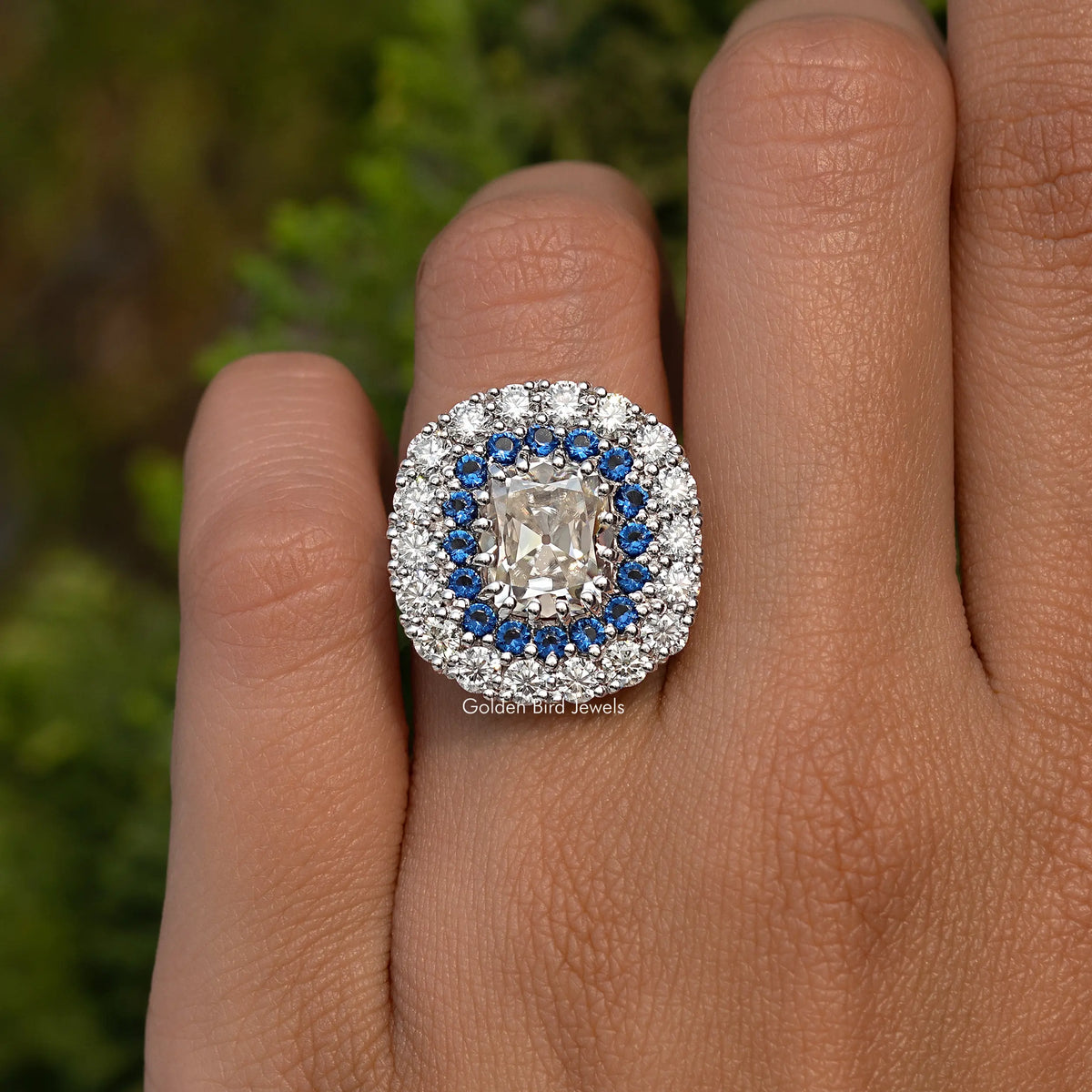 Cushion moissanite ring with double halo: white stones and blue accents, on hand