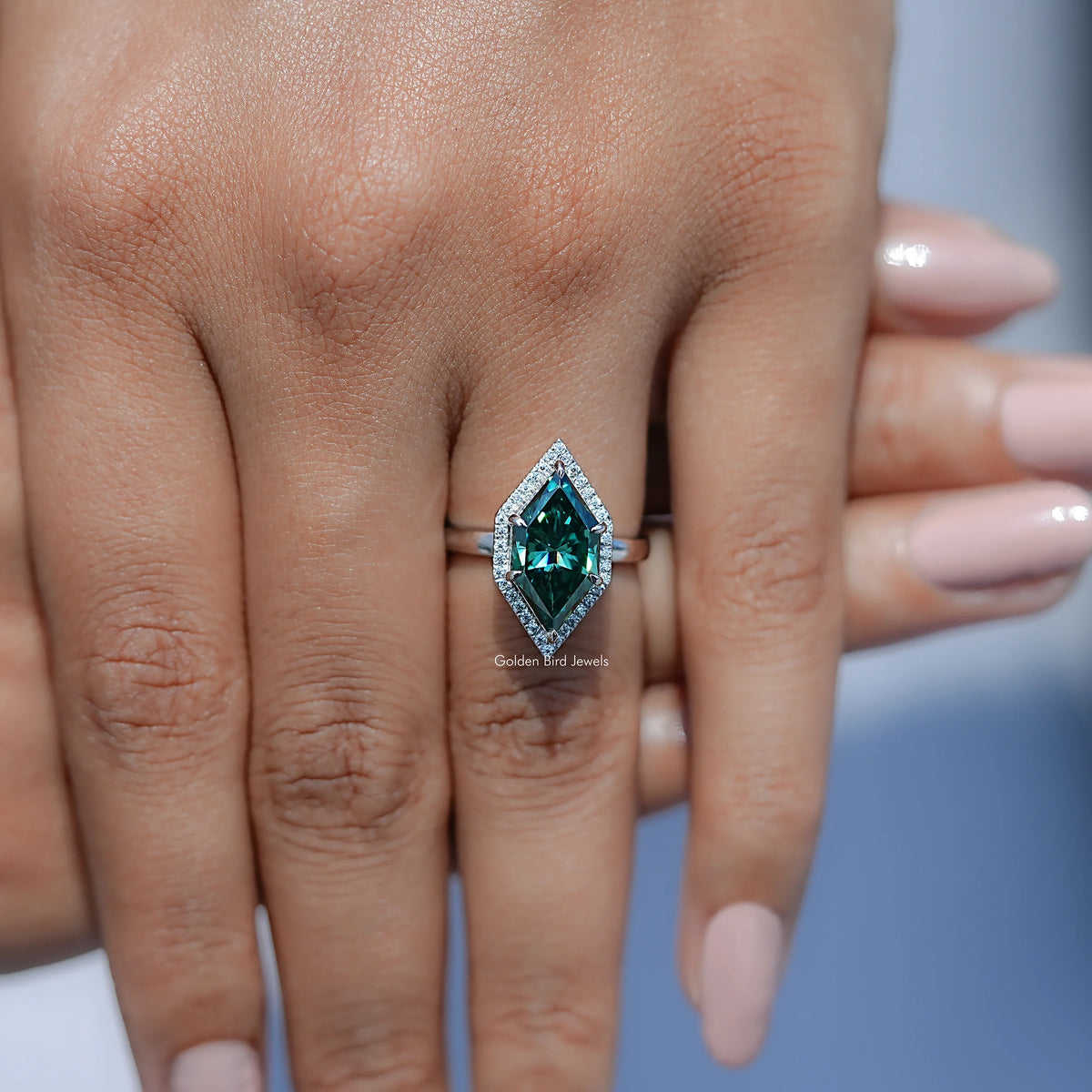 Teal marquise halo engagement ring with rectangular center stone, shown on finger