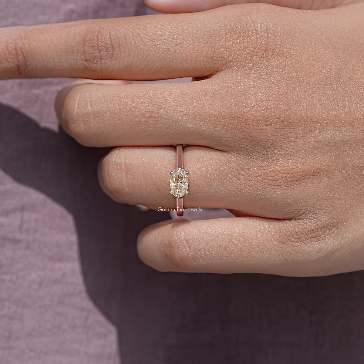 Oval cut moissanite solitaire ring with four prongs on finger.