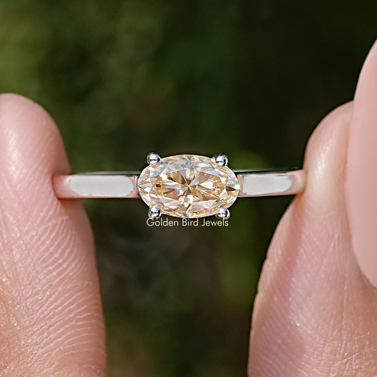 Close-up of oval cut moissanite solitaire ring with four-prong setting and band.