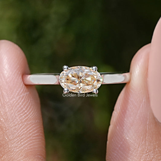 Close-up of oval cut moissanite solitaire ring with four-prong setting and band.