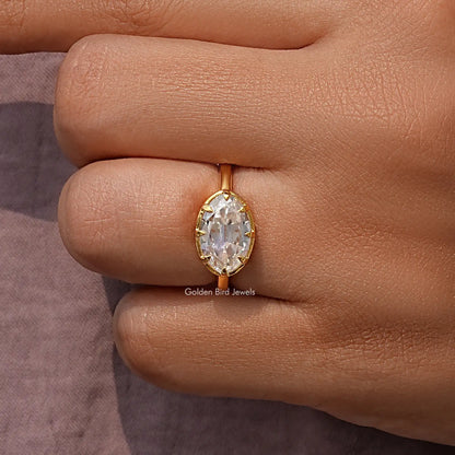 Oval moissanite solitaire ring close-up on knuckle, gold-tone band and bezel prongs.