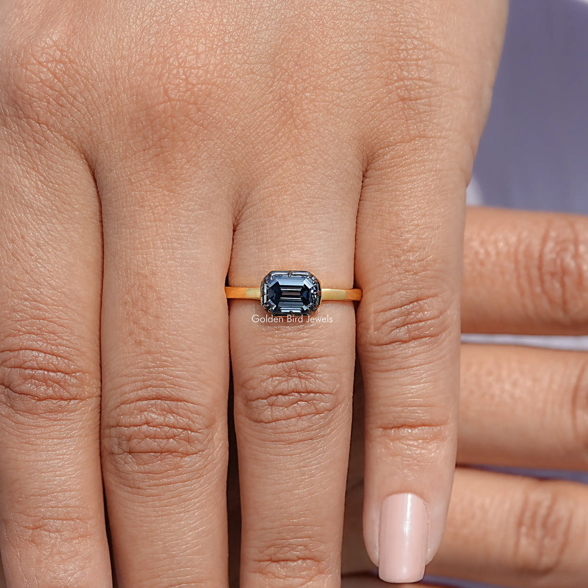 Gold solitaire ring with emerald-cut gemstone, worn on finger