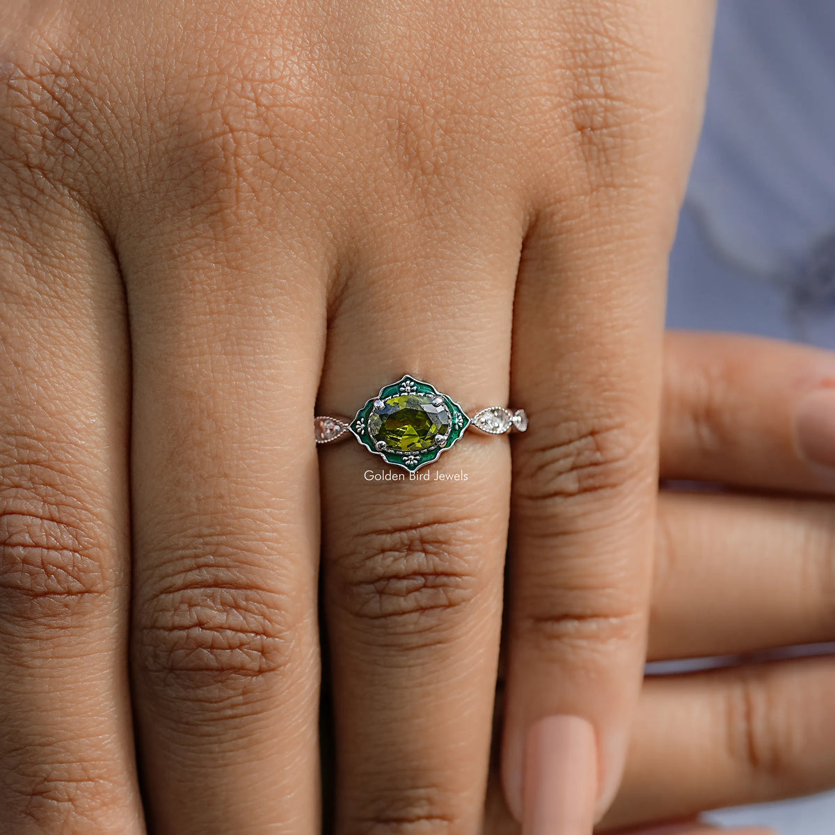 Oval green gemstone ring with diamond halo and side stones on a hand
