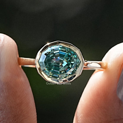 Front view of Blue Green Moissanite Step Cut Oval Solitaire Ring in two fingers 
