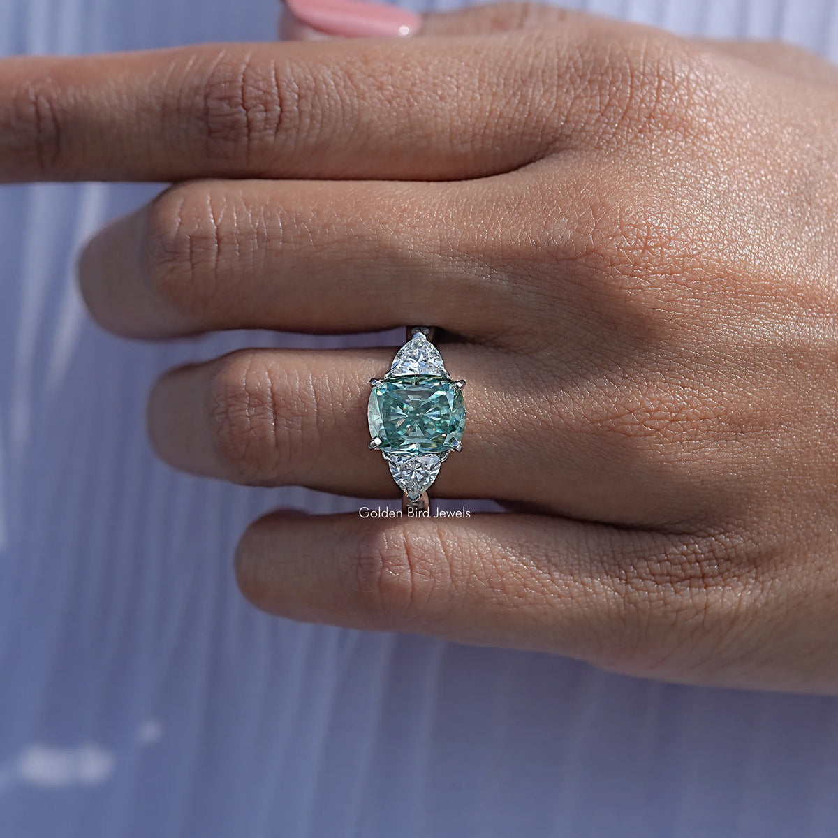 Argentium silver three-stone engagement ring with cushion-cut moissanite center, finger shot