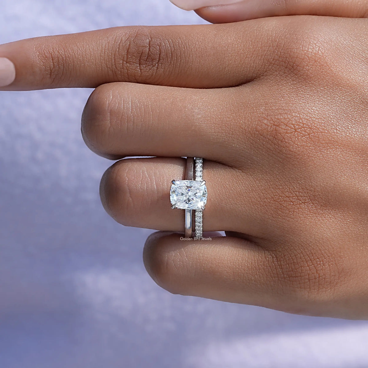 Silver-tone ring on finger with small cushion moissanite and vertical side stones
