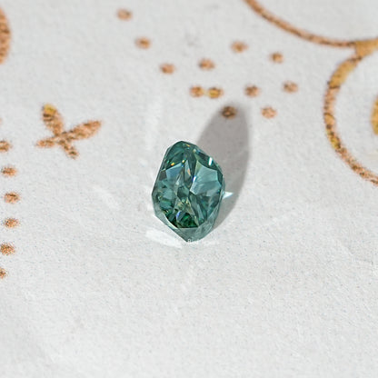 Elongated teal-green moissanite stone, angled view with sharp facets.