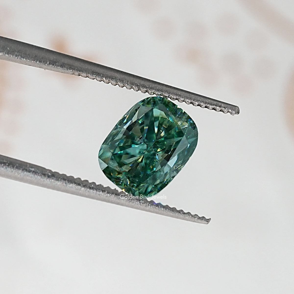 Oval cushion teal-green moissanite stone, held by metal tweezers.