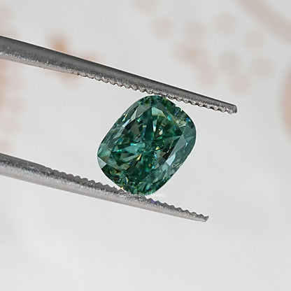 Oval cushion teal-green moissanite stone, held by metal tweezers.