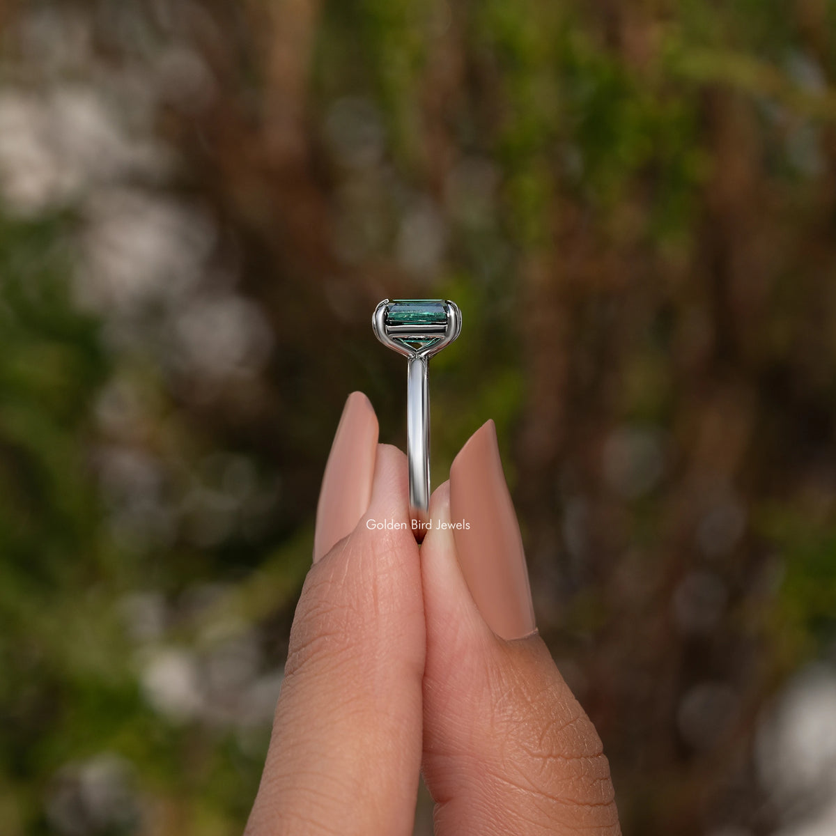 Two-stone ring viewed from the top, featuring a green emerald-cut center stone
