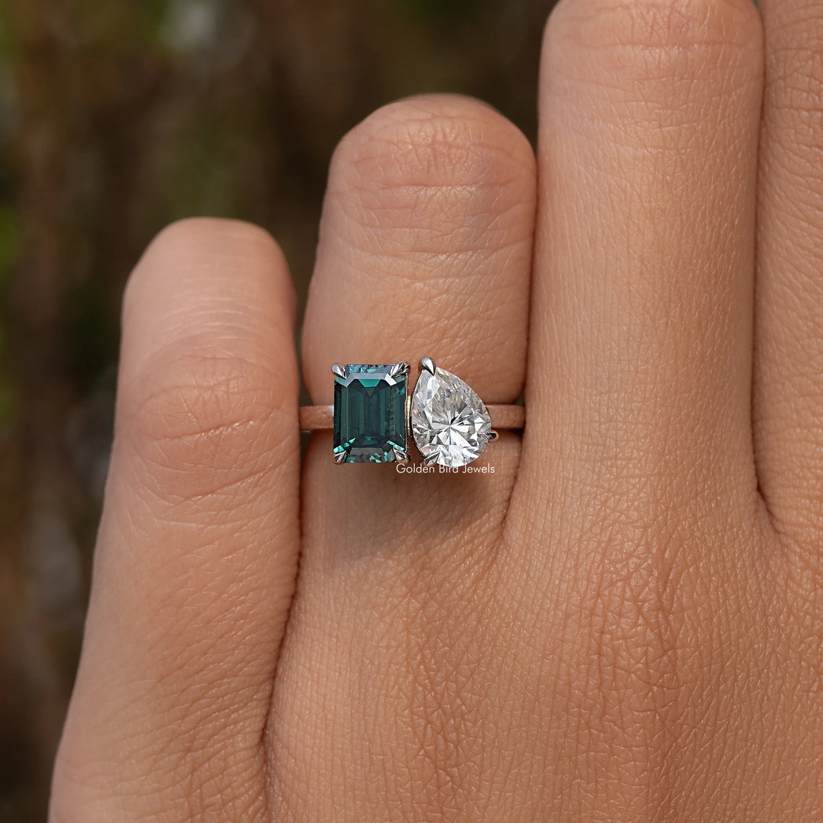 Three-stone-style ring on finger: emerald-cut green center with round pear side