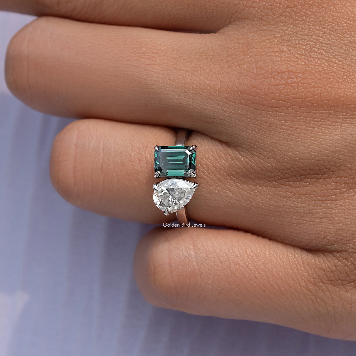 Close-up of emerald-cut green center stone with pear-cut clear side stone