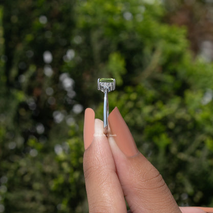 Silver ring showing emerald-cut green stone and four-corner prongs, slim band