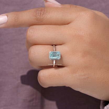 Close-up of blue emerald-cut moissanite solitaire in silver bezel setting