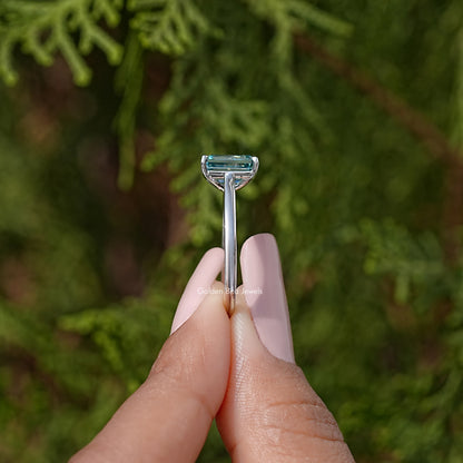 Emerald-cut moissanite solitaire ring side view with teal gemstone and prongs