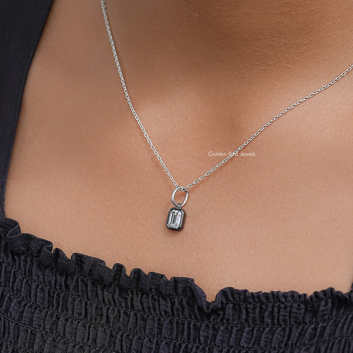 Rectangular solitaire pendant on thin silver chain over black ruffled top