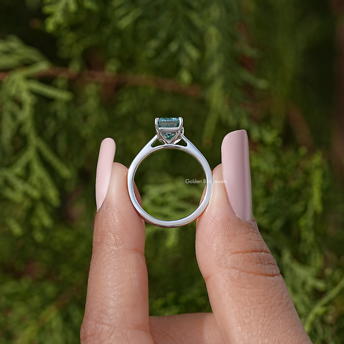Emerald-cut moissanite solitaire ring back view with teal stone in silver halo