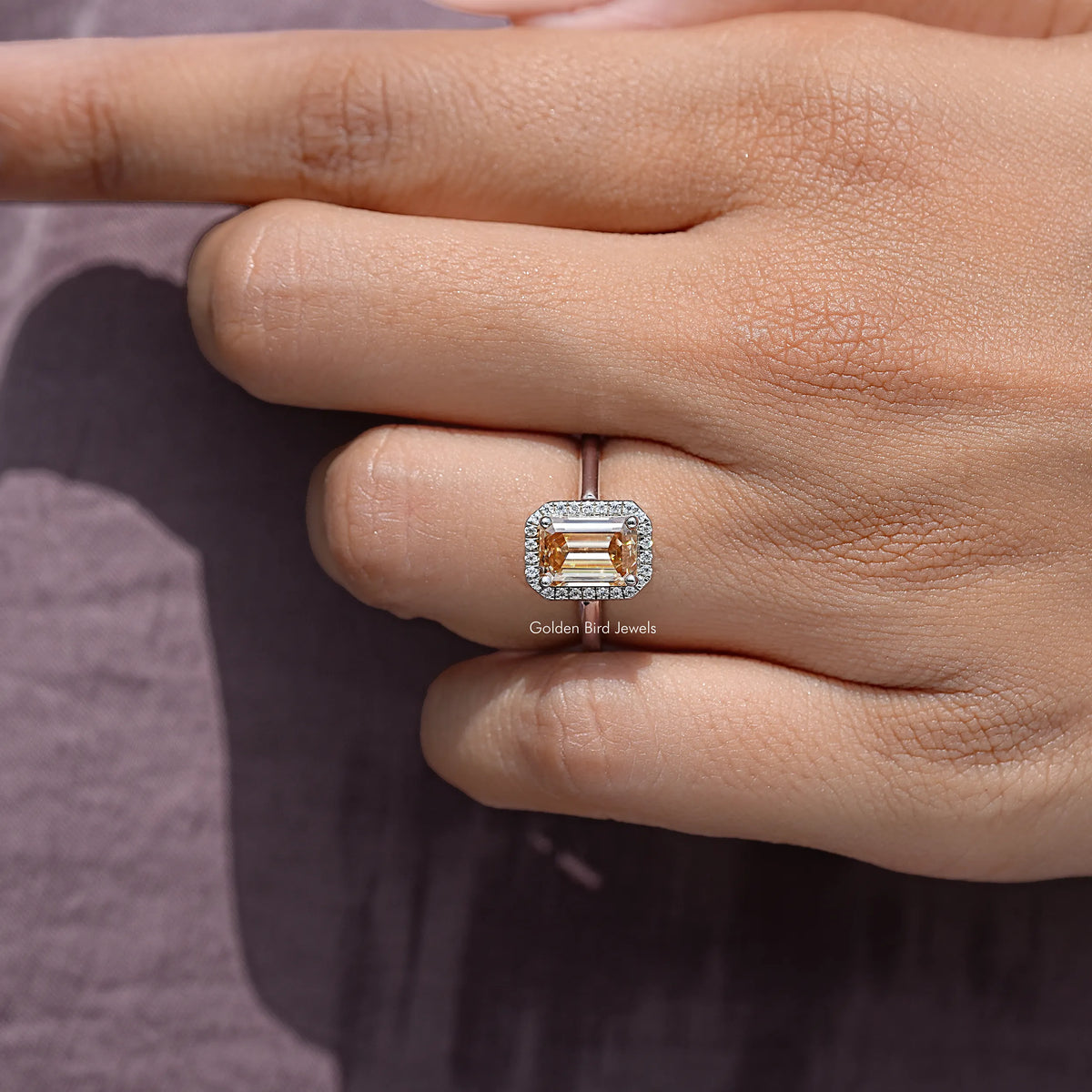 Sterling silver halo engagement ring with emerald-cut center stone, side view on finger