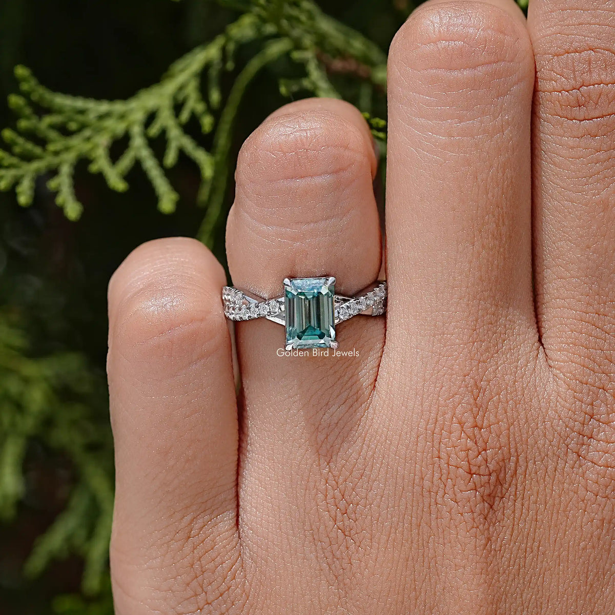 Teal emerald-cut moissanite wedding ring on twisted silver band, close-up