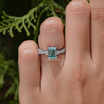 Teal emerald-cut moissanite wedding ring on twisted silver band, close-up