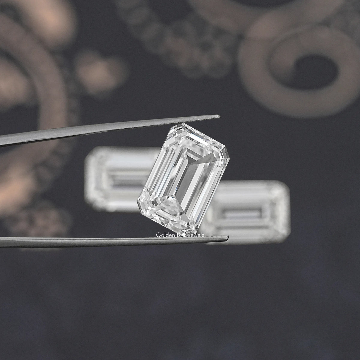 Emerald-cut lab diamond held in metal tweezers, clear faceted step-cut stone.