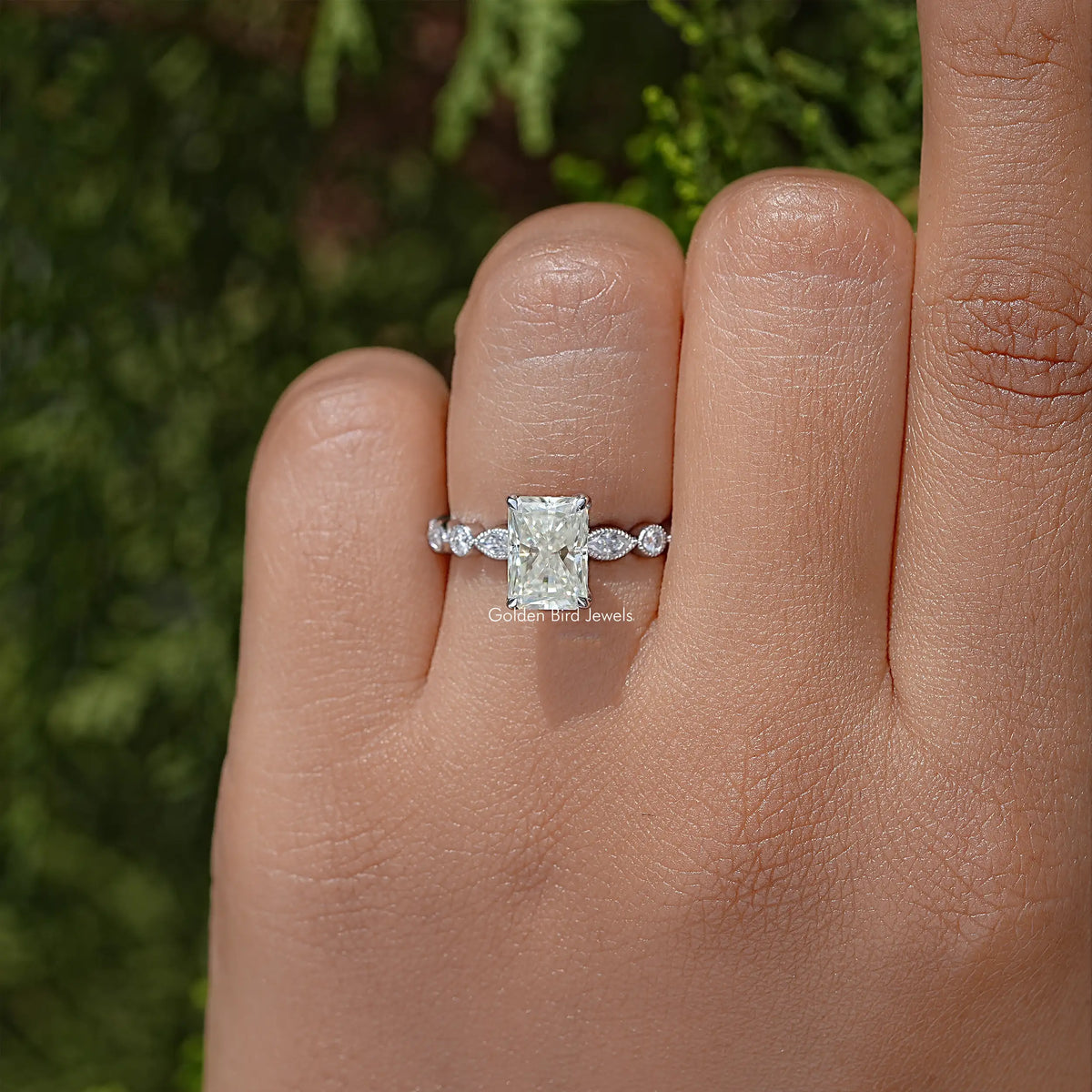 Radiant cut moissanite engagement ring on hand, square center stone with two side stones